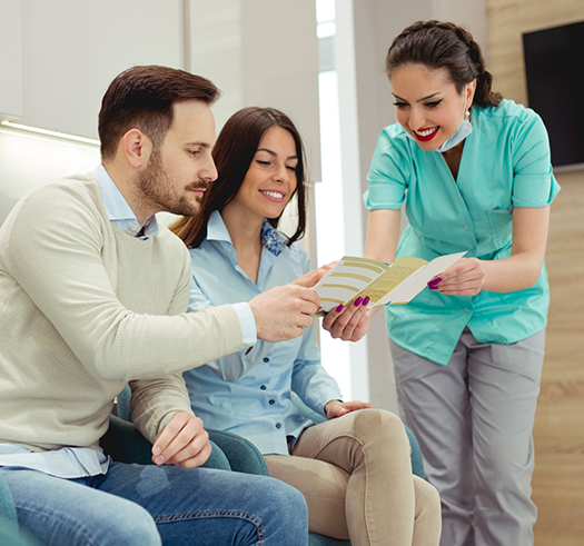Dental team member showing a pamphlet to two patients