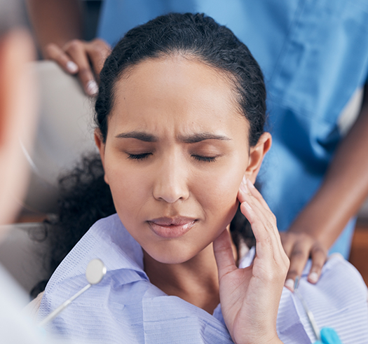 Woman in the dental chair wincing and holding her cheek in pain