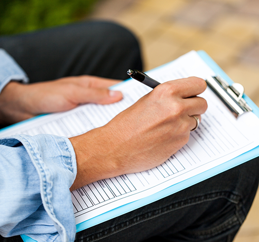 Person filling out paperwork on a clipboard