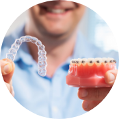 Smiling man holding a clear aligner and a model of the mouth with braces
