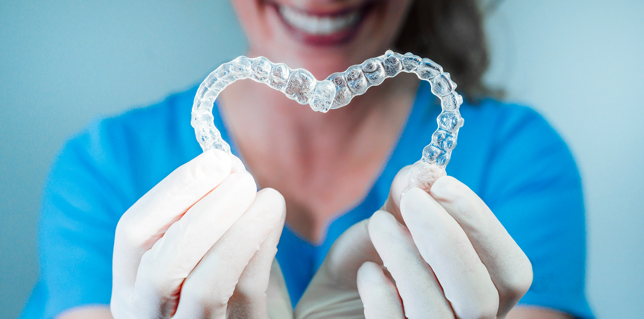 Smiling orthodontist making a heart shape with two Invisalign clear aligners in Bartlett