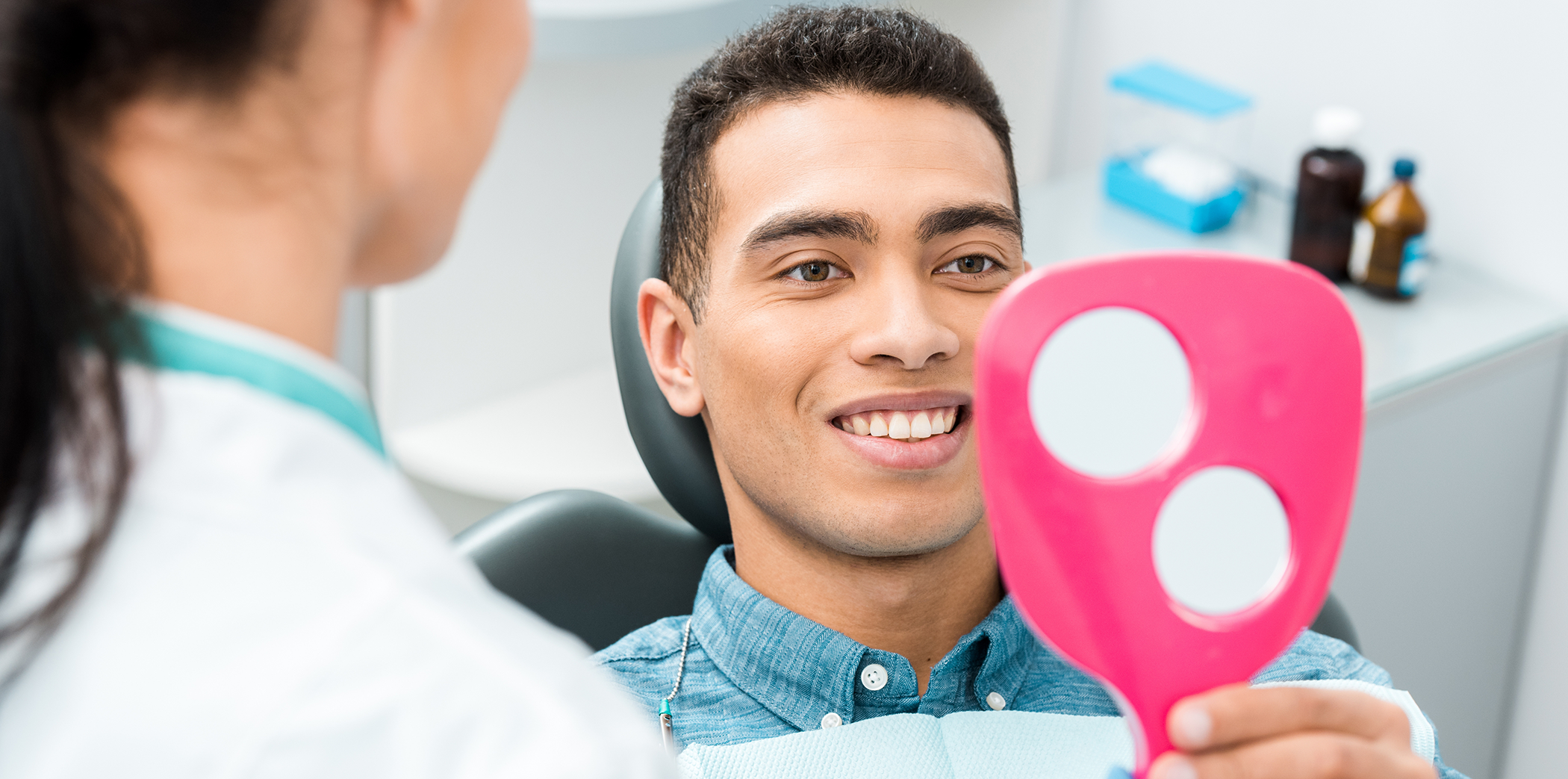 Dental patient looking at his smile in a mirror after replacing missing teeth in Bartlett