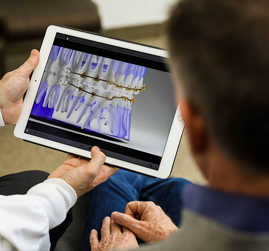 Orthodontist showing a patient a tablet with a digital illustration of how braces move the teeth