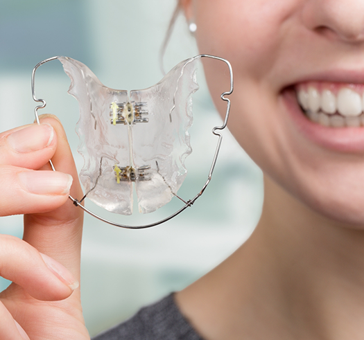 Person smiling while holding a wire retainer