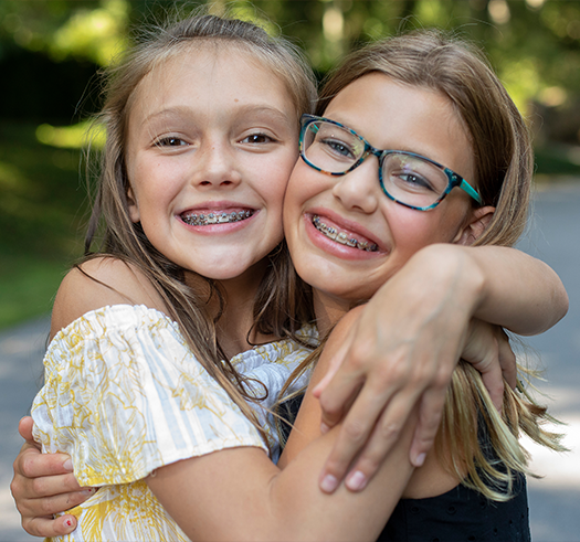 Two girls with traditional braces smiling and hugging