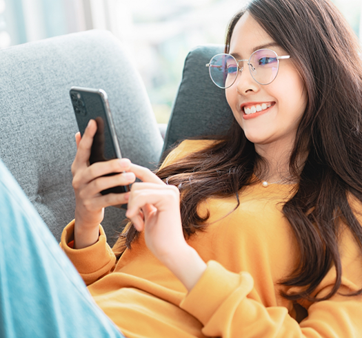 Woman laying on a couch and smiling at her phone