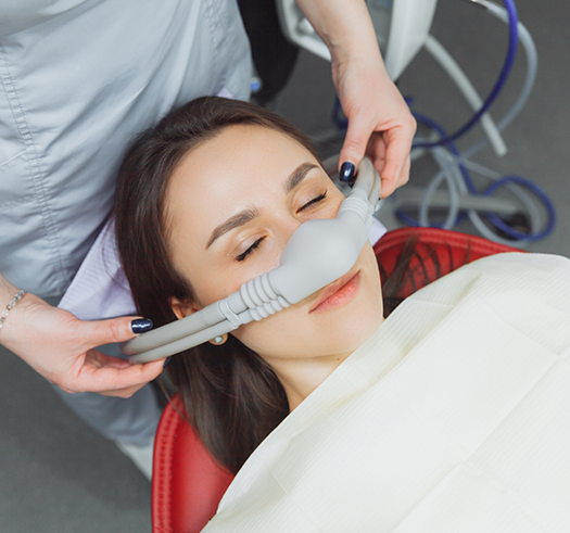 Woman in the dental chair with her eyes closed and a nitrous oxide mask over her nose